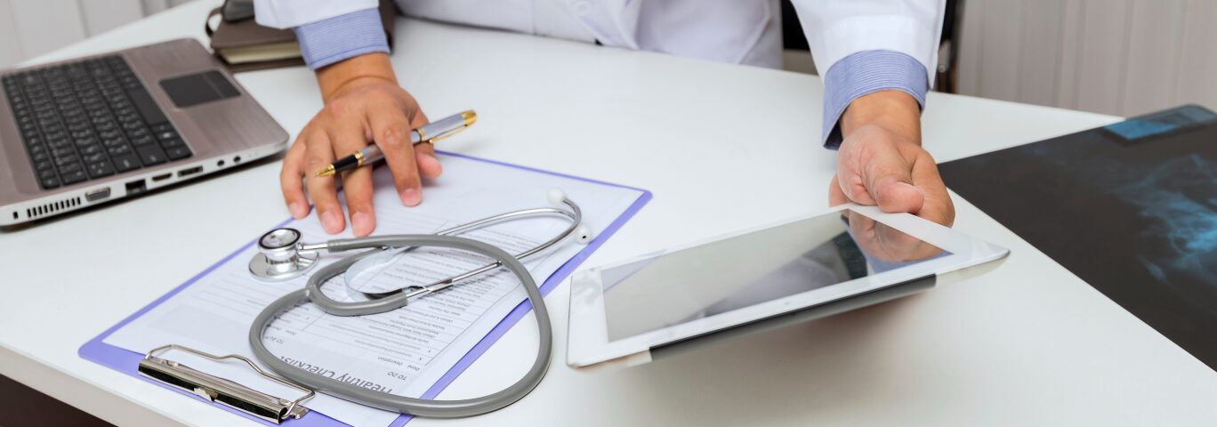 ein Arzt sietzt an seinem Schreibtisch und kontrolliert Daten über sein IPad